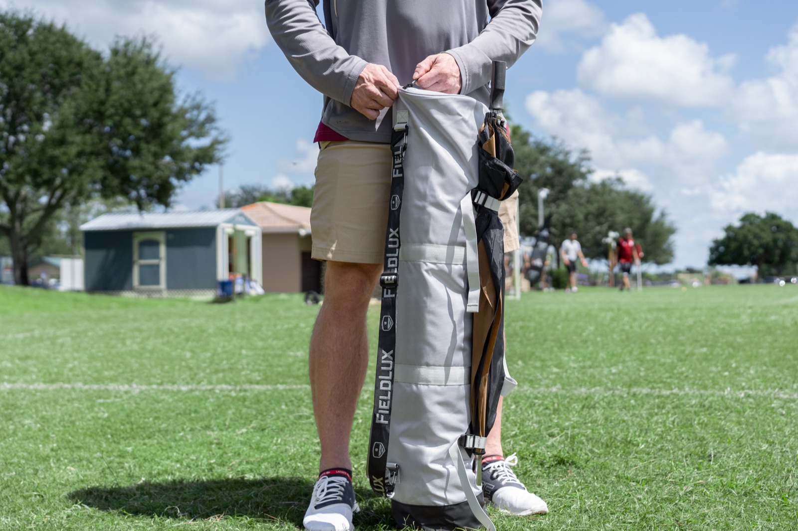 A FieldLux Chair Bag with an umbrella secured under the external cinch straps, on a soccer field sideline.